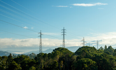 Landscape with electricity poles and high voltage lines in harmony with nature on a blue sky...