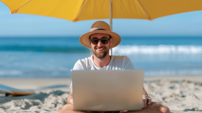 Freelancer working on a laptop under a beach umbrella with ocean view. Relaxed work environment on the beach, laptop in hand, surfboard nearby.