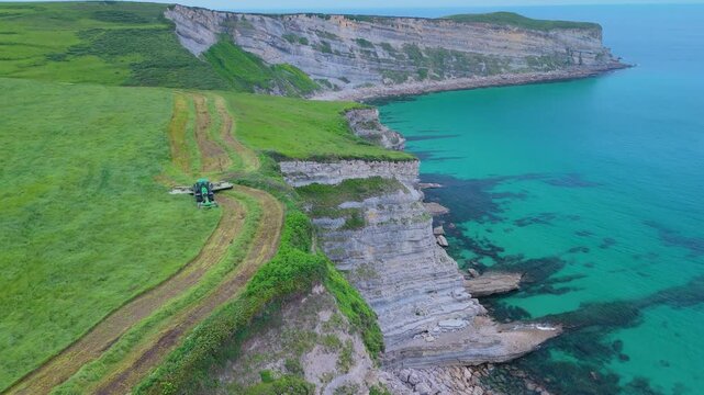 Tractor mowing the grass in the area of ​​Punta Ballota on the coast of Tagle. Aerial view from a drone. Arnuero Municipality. Cantabrian Sea. Cantabria. Spain. Europe