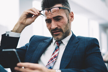 Mature successful entrepreneur dressed in formal wear reading banking notification on smartphone...