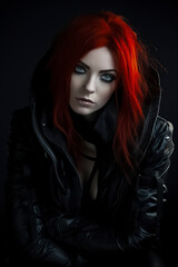 Portrait of woman with red hair and black leather jacket on a dark background. Studio photography. Gothic and alternative fashion concept