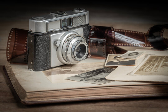 VINTAGE CAMERA AND NEGATIVE FILM ROLLS ON A PHOTO ALBUM WITH BLACK AND WHITE PHOTOGRAPHS AND PORTRAITS.