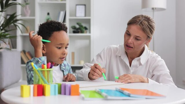 Adorable little african american boy with curly hair having fun at pediatric specialist appointment, happy child drawing with female therapist, exercises for children with autism.