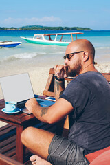 Pensive male freelancer thinking about idea for new article recreating on ocean shore with laptop computer,businessman using netbook with mock up screen for remote job during vacation on resort