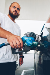 Serious bearded hipster guy filling talk of automobile for driving holding hose and nozzle on service station,young male owner of car refill vehicle with petroleum, climate pollution concept