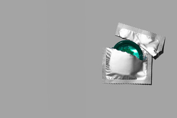 Condom half out of package on a grey background. A condom use to reduce the probability of pregnancy or sexually transmitted disease (STD). Safe sex and reproductive health concept. Top view.