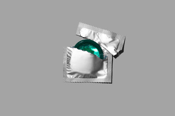 Condom half out of package on a grey background. A condom use to reduce the probability of pregnancy or sexually transmitted disease (STD). Safe sex and reproductive health concept. Top view.