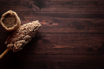 Organic whole Pearl Millet (Pennisetum glaucum) or Bajra seeds in a jute bag with Sorghum seeds (Sorghum bicolor), isolated on a dark wooden background. Top view.