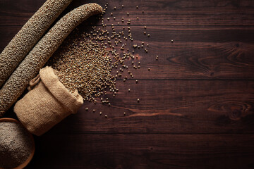Organic whole Pearl Millet (Pennisetum glaucum) or Bajra seeds spilled out from a laying jute bag with Bajra Flour, isolated on a dark wooden background. Top view.