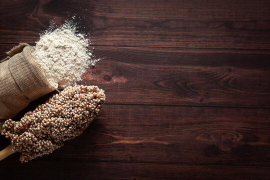 Organic Sorghum Flour (Sorghum bicolor) spilled out from a jute bag with seeds, isolated on a dark wooden background. Top view.