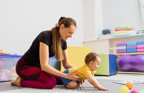 Physical therapist assisting young child with damage to nervous system at rehabilitation center during daytime. Specialist aids little boy in body motor skill development