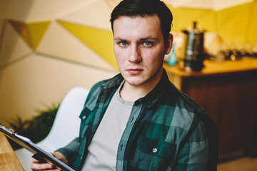 Portrait of young casually dressed male learning information for college exams holding folder,serious male looking at camera making planning for startup checking documents in coworking space