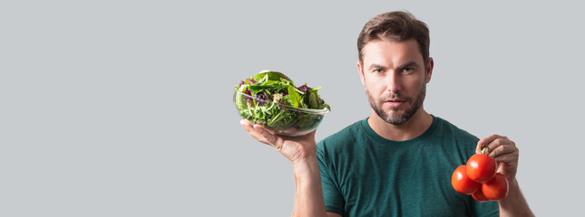 Portrait of a man hold a salad with greens Portrait of a man eating a salad. Healthy food. Man hold fresh tomato and vegetable salad isolated on gray background, studio portrait. Wide banner of