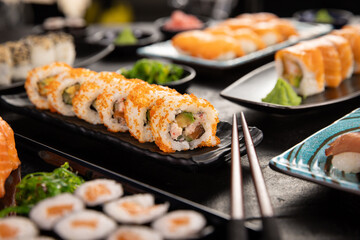 Top view of traditional japanese cuisine . Sushi rolls set with salmon , tuna fish and vegetable served on black stone table . Asian food on black stone slate with chopsticks .
