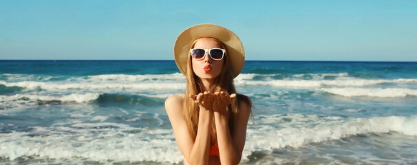 Summer vacation, beautiful young woman blowing kiss in bikini swimsuit, tourist hat on beach on sea