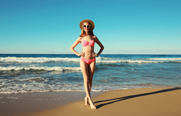 Summer vacation, beautiful happy slim woman in pink bikini swimsuit, tourist hat on the beach on sea
