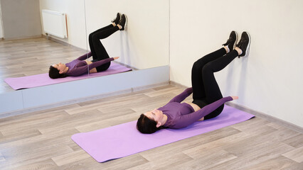 Athletic 30 year woman does abdominal crunches leaning her feet with bent knees into the wall lying...