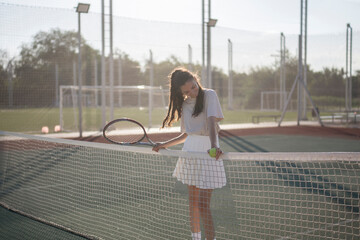woman holds a tennis racket while standing near the net on the court on a sunny day outdoor