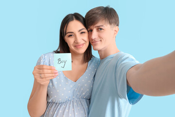 Young pregnant couple holding paper with word BOY on blue background