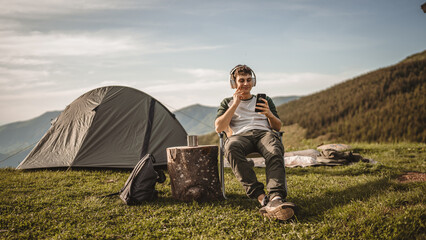 Young boy sit on chair on the mountain listen music on headphones