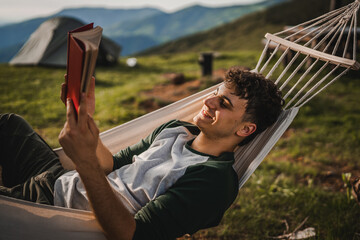 Young boy lying down in a hammock on the mountain and read a book