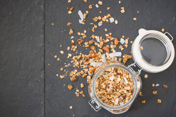 Glass jar of homemade organic granola with coconut and pecans on black background. Delicious breakfast cereal. Healthy muesli.