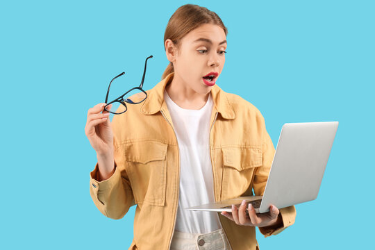 Shocked female programmer with eyeglasses and laptop on blue background