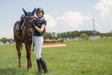 A young girl stands next to a horse before an equestrian competition. 