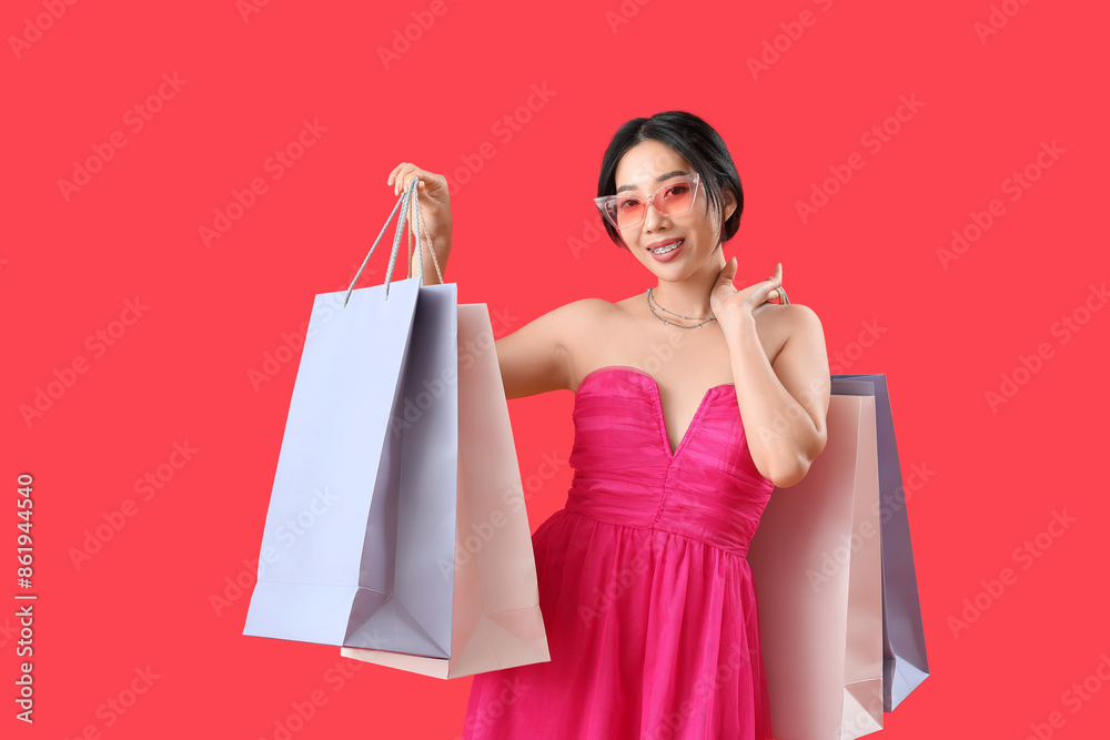 Poster Happy beautiful young Asian woman with shopping bags on red background