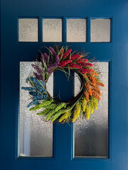 Pride rainbow flower wreath on the blue door with frosted glass windows

