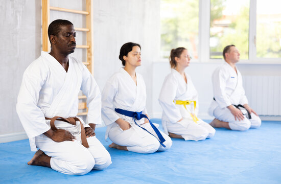 Calm middle-aged male attendee of karate classes sitting in seiza position in group during workout session