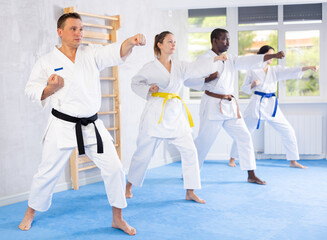 Kata karate teacher conducts classes and performs movements and fighting techniques together with cosmopolite students to prepare them for competitions.