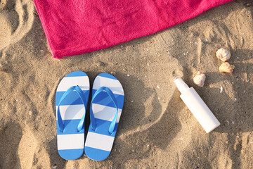 Bottle of sunscreen cream, flip-flops and towel on sand