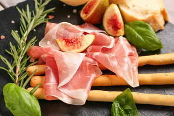 Board with slices of tasty prosciutto, basil, Italian Grissini and figs on table