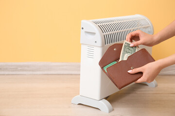 Female hands holding wallet with money near electric convector heater at home. Heating saving concept