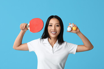 Sporty young Asian woman with ping-pong racket and balls on blue background