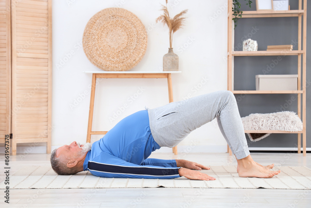 Wall mural Sporty mature man doing yoga on carpet at home