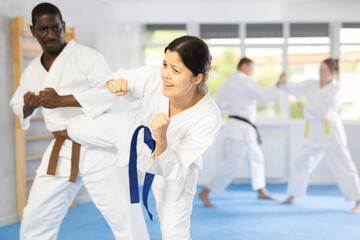 Fototapeta premium Active middle-aged woman attendee of karate classes practicing fighting techniques during workout session