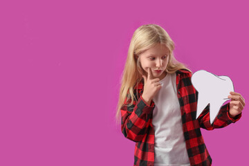 Thoughtful little girl with healthy teeth and paper tooth on purple background