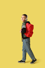 Fototapeta premium Cute schoolboy with headphones and backpack on yellow background