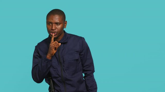 Security guard doing shush sign gesturing with finger, preventing public access in restricted area. Portrait of stern bodyguard urging people to keep quiet, studio background, camera A