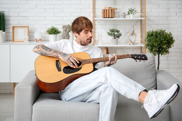 Cool tattooed young man playing guitar at home