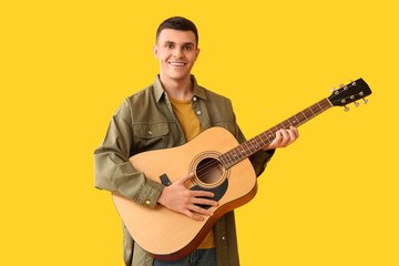 Obraz premium Handsome young man playing guitar on yellow background