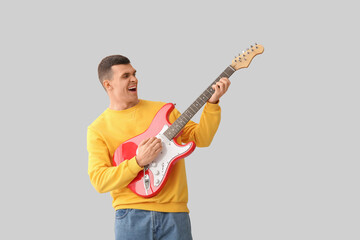 Cool young man playing electric guitar on light background