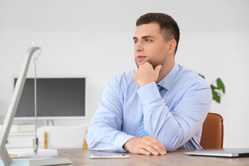 Naklejka premium Thoughtful young businessman pondering business strategy and future decisions in a modern office environment, he is focused on his thoughts, with his hand resting on his chin
