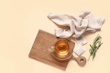 Wooden board with glass cup of hot rosemary tea on beige background