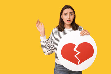 Beautiful young displeased woman with heart dislike icon on yellow background