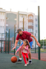 Dad plays basketball on equal terms with his little daughter, picking up the ball in a fight....