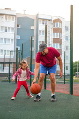 The child is having fun playing basketball with his father in the yard on a warm summer day. Sports...