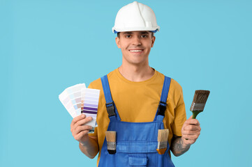 Young painter with color palettes and paint brush on blue background